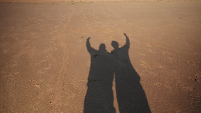 couple heart silhouettes, couple stretching their arms and forming hearts at sunset on beach