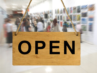 An "Open" sign against a blurred background of an interior with people