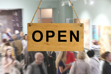 An "Open" sign against a blurred background of an interior with people