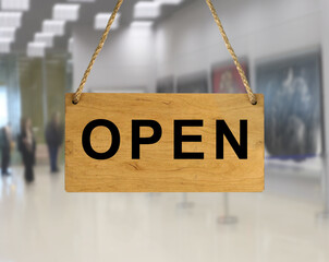 An "Open" sign against a blurred background of an interior with people