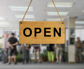 An "Open" sign against a blurred background of an interior with people