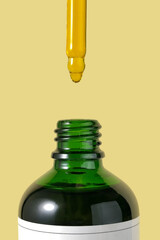 Close up view of Cosmetic oil dripping from pipette in a small bottle.