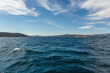 Obraz premium View from the open sea towards Croatian islands on a sunny day with blue water, distant hills, and light clouds in the sky