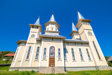 Romanian Orthodox church in Maramures displaying traditional architecture with numerous spires and intricate stained glass windows, standing against a clear vibrant blue sky in Romania