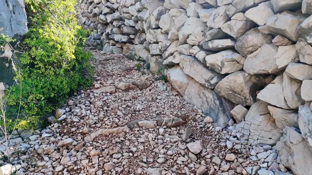 Sunlit stone pathway winding through rustic rock walls with green foliage accents