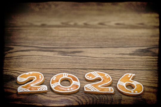 Sweet baked happy New year 2026 gingerbreads on vintage wooden background with black border. Close-up ornate Christmas cookies in numerals shape on dark brown natural wood texture in retro still life.