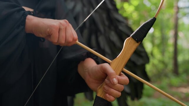 Close up of hands gripping wooden bow and drawing arrow in green forest, sunlight reflecting on polished wood, capturing tension, focus, and calm strength in moment before release