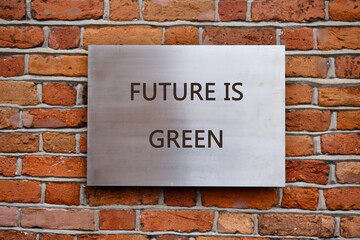 A metallic sign reading FUTURE IS GREEN affixed to a vintage red brick wall, highlighting the importance of ecology and sustainable progress