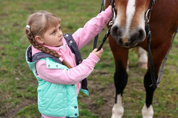 Obraz premium Equine assisted therapy. Little girl stroking beautiful horse in countryside. Lovely domesticated pet