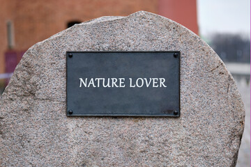 A large Granite Rock with a black metal plate affixed to it. The plate displays the words NATURE LOVER in capital letters. This is likely a monument or memorial in a park