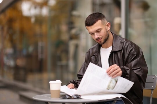 Young man reading newspaper at table in outdoor cafe. Space for text