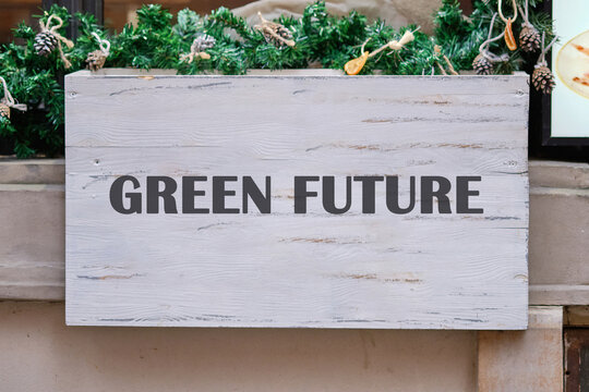 A white wooden sign is adorned with festive greenery and pinecones. Bold, dark text reads GREEN FUTURE, suggesting a focus on environmental sustainability and ecological awareness - Powered by Adobe