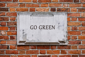 Fototapeta premium A GO GREEN message is displayed on a weathered stone tablet, set into a textured red brick wall, suggesting a commitment to eco-friendly practices