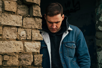 Obraz premium A man leans against a weathered brick wall deep in thought The setting has a melancholic vibe with soft lighting casting shadows around him creating an introspective atmosphere