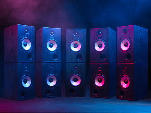 Group of sound speakers stacked on top of each other in neon lighting and light haze.