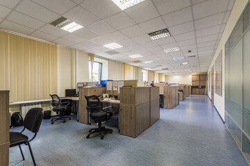 Spacious office features multiple cubicles equipped with computers and ergonomic chairs. Natural light filters through large windows