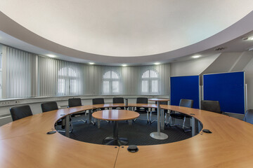 Meeting room of a modern office with a large round table and blinds on arched windows.