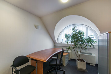 The interior of a small office space with an arched window and work furniture.