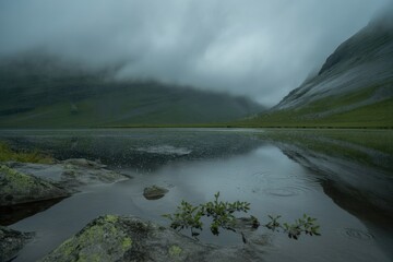 Moody mountain lake with rain falling on water and misty clouds nature landscape