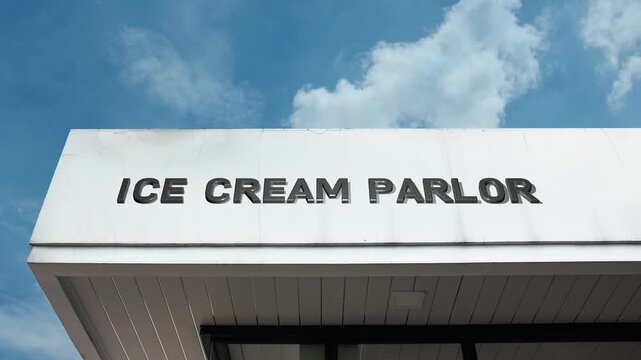 Ice Cream Parlor word sign clearly displayed on the commercial retail building facade beneath a clear blue sky, signifying a shop specializing in selling frozen desserts and sweet treats.