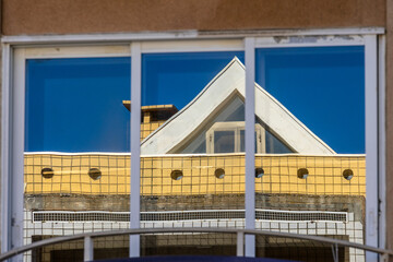 Reflection of modern yellow building with triangular roof in window glass, Portugal, Ovar – Furadouro, 9.10.2025