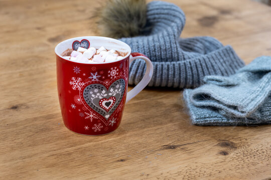Mug of hot chocolate with marshmallows on a wooden table, with a booble hat and gloves, close up. A nice warm, cosy feeling.