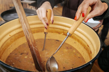A steaming bowl of hearty soup is served from a large pot outdoors, offering warmth and comfort during a cozy autumn gathering.