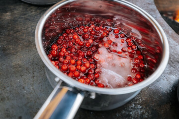 Close-up of lingonberries simmering in stainless steel pots over an open fire, bubbling as they transform into jam during an outdoor cooking session.