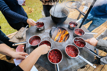 People cook lingonberries in small pots over an open fire during an outdoor jam-making workshop,...