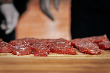 Close-up of raw beef steaks seasoned with salt and pepper, laid out on a wooden cutting board, ready for grilling at an outdoor cooking event.