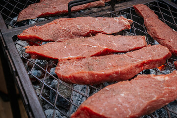 Close-up of raw beef steaks sizzling on a grill over hot coals, with visible seasoning and sear marks beginning to form.