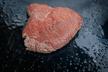 Four juicy steaks sear on a sizzling hot flat grill beside open flames, cooking in their own juices with a perfect crust forming on the surface.