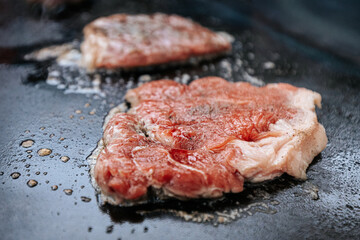 Four juicy steaks sear on a sizzling hot flat grill beside open flames, cooking in their own juices with a perfect crust forming on the surface.