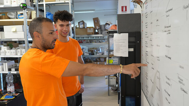 Collaborative shift planning meeting between workers in warehouse in front of planning board