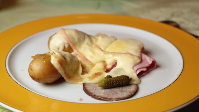Une assiette de raclette accompagn&eacute;e de charcuterie et de pommes de terre.