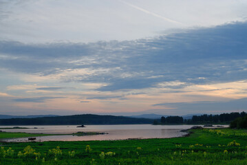 Beautiful atmospheric sunset with warm orange and pink hues, illuminating the sky and landscape in soft glowing light.