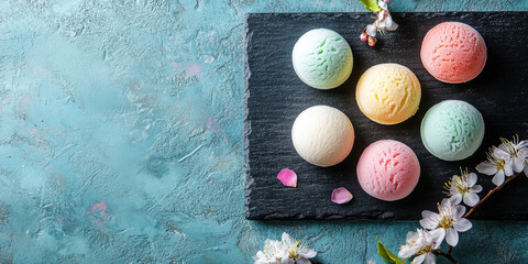 Assorted mochi ice cream scoops in pastel shades decorating a dark slate serving board, contrasting with delicate white cherry blossoms and decorative pearls