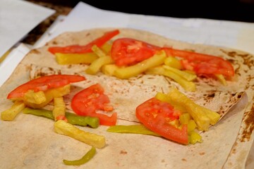 Preparation of meat döner wrap, a traditional Turkish street food. The döner is cooked over a wood fire and wrapped in lavash with potatoes, pickled peppers, and tomatoes. Turkish fast food.