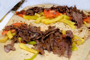 Preparation of meat döner wrap, a traditional Turkish street food. The döner is cooked over a wood fire and wrapped in lavash with potatoes, pickled peppers, and tomatoes. Turkish fast food.