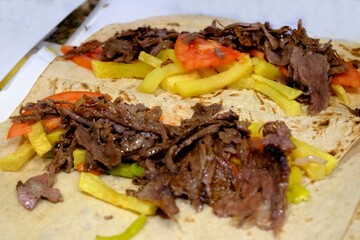 Preparation of meat döner wrap, a traditional Turkish street food. The döner is cooked over a wood fire and wrapped in lavash with potatoes, pickled peppers, and tomatoes. Turkish fast food.
