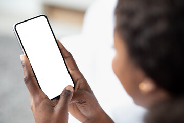 A black woman sits in her bedroom, holding a brand new smartphone with an empty screen. She is just waking up and exploring the newest mobile applications, with a blurred background.