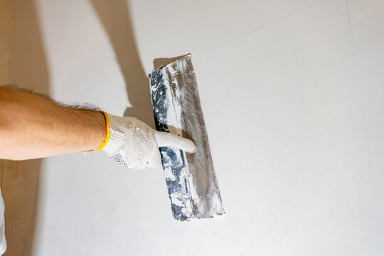 Gloved worker actively spreads white spackling compound with a finishing tool, preparing the textured wall for a final coat. - Powered by Adobe