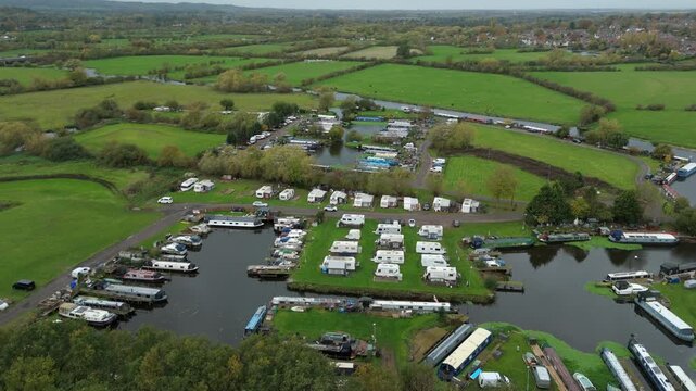 Aerial shot of holiday home caravans mobile camping site near river lock system, canal boats barges and rolling green fields near Sileby, England, UK