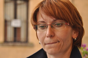 Woman with glasses looking thoughtfully outdoors in a quiet setting, showcasing reflection and...