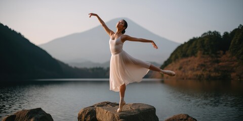 Asian female ballerina dancing gracefully by mountain lake at sunset
