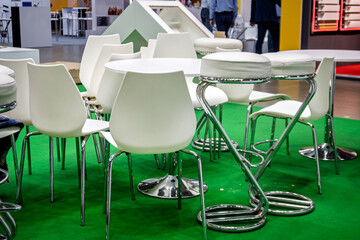 Modern white chairs and tables with chrome details on a vibrant green carpet, set in an exhibition...