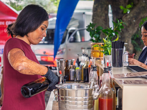Close-up shot of a Latina entrepreneur with burn scars on her face and body preparing a michelada behind the counter. 