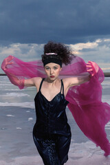 A girl with a red shawl poses against a natural backdrop