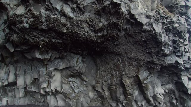 A detailed close up shot of a towering basalt column formation in Iceland. The hexagonal columns, formed by the rapid cooling of lava, create a unique and dramatic natural texture. The scene highlight