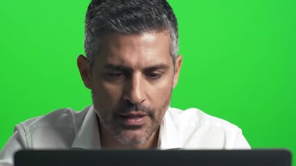 Closeup of a focused man with graying hair working intently on a laptop against a vibrant green screen background ideal for compositing and virtual sets.